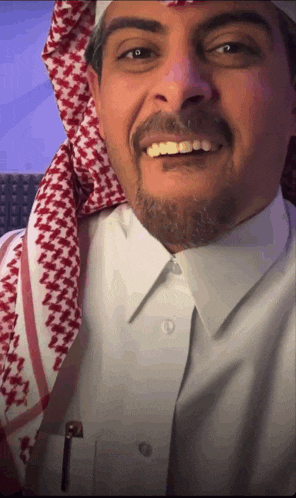 a man wearing a white shirt and a red and white scarf smiles at the camera