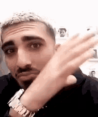 a man with a beard is wearing a watch on his wrist and making a funny face .