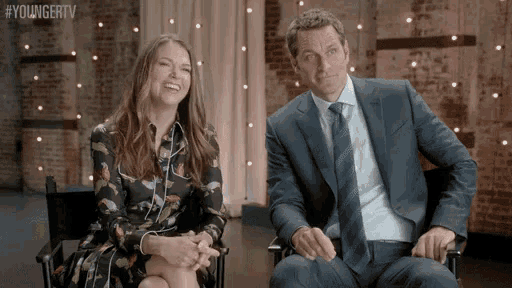 a man and a woman are sitting next to each other in chairs and smiling .