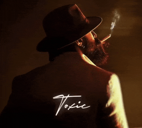 a man with a beard is smoking a cigarette and the word toxic is on the back of his jacket