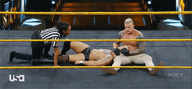 a man is laying on the ground in a wrestling ring while a referee looks on ..