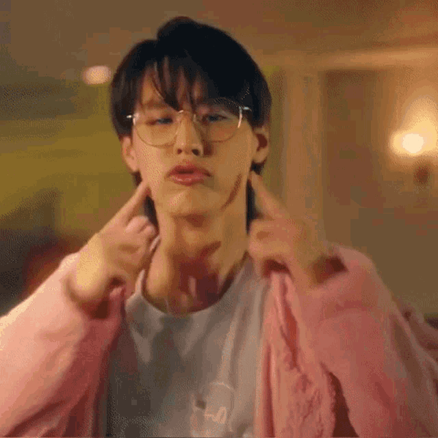 a young man wearing glasses and a pink jacket is making a face .