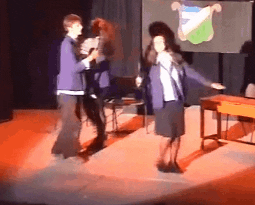 a group of people are dancing on a stage in front of a banner with a crest