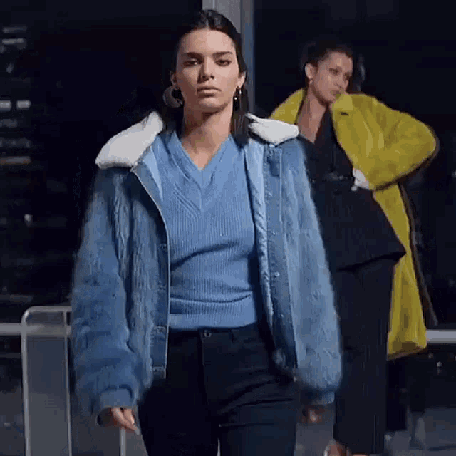 a model wearing a blue sweater and a blue fur jacket is walking down the runway .