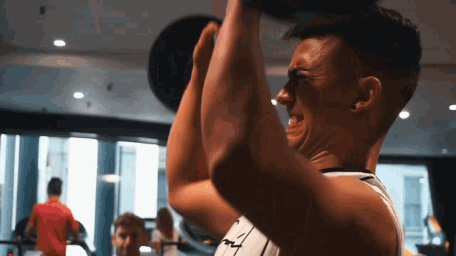 a man in a white tank top is lifting a heavy object over his head