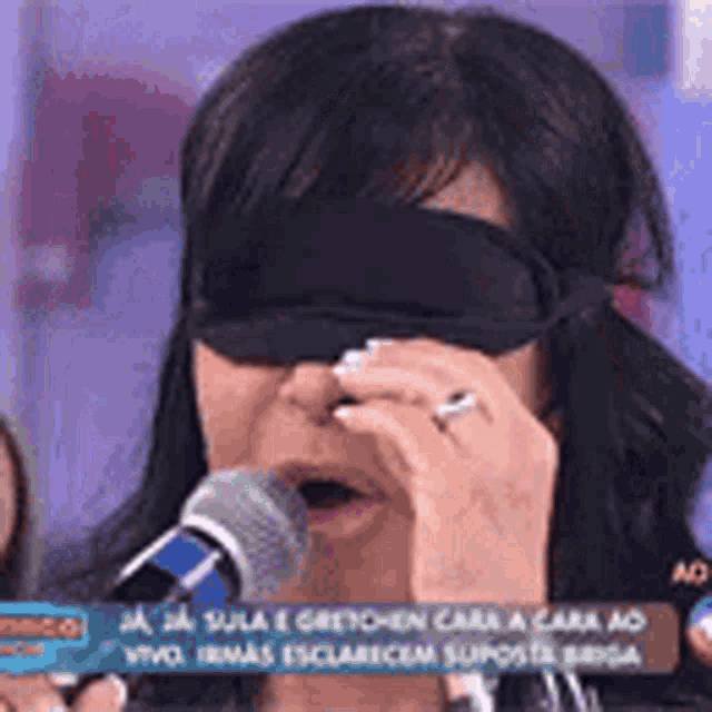 a woman wearing a blindfold and a ring is holding a microphone .