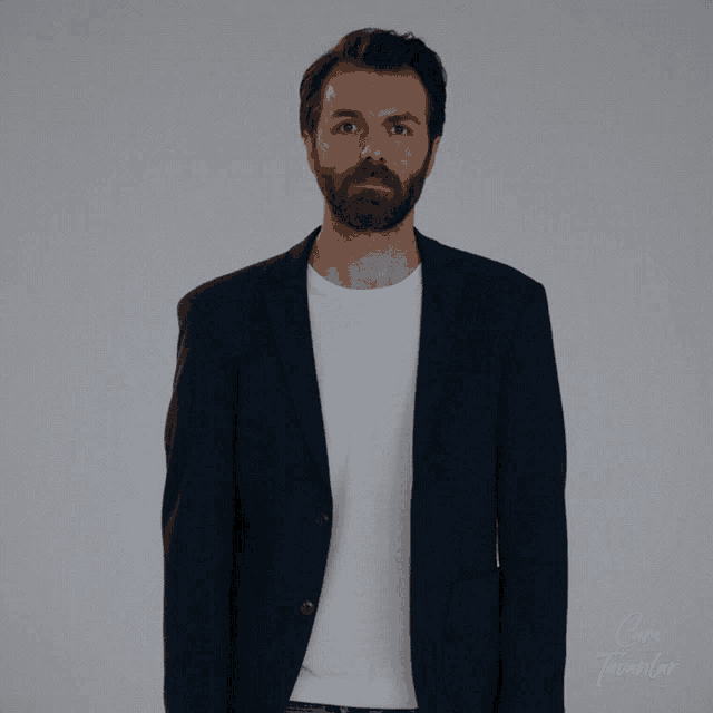 a man with a beard is wearing a blue jacket and a white t-shirt with the word cam on the bottom