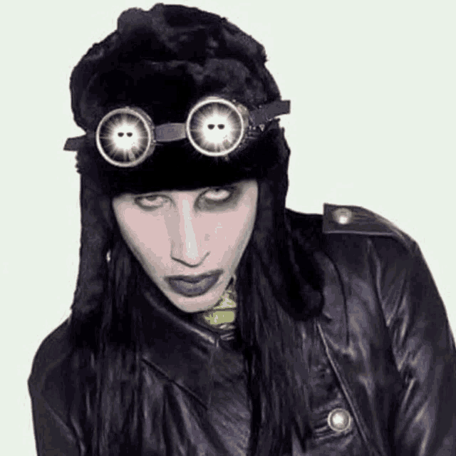 marilyn manson is wearing a black hat and goggles and a leather jacket .