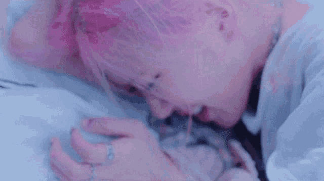 a woman with pink hair is laying on a bed and drinking from a straw .