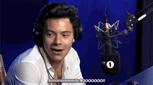 harry styles is wearing headphones and talking into a microphone in front of a blue wall .