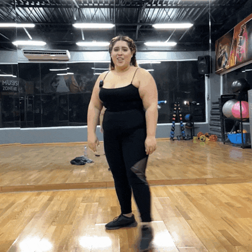 a woman stands in front of a mirror in a gym with a sign that says music zone