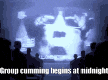 a group of people looking at a screen that says " group cumming begins at midnight "