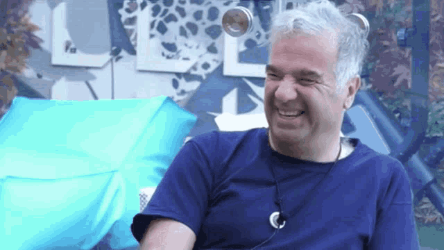 a man in a blue shirt with a necklace around his neck is laughing