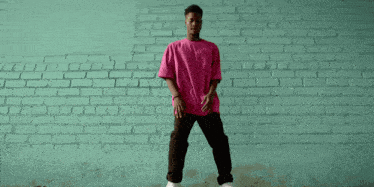 a man in a pink shirt is dancing in front of a brick wall with the letters tr painted on it