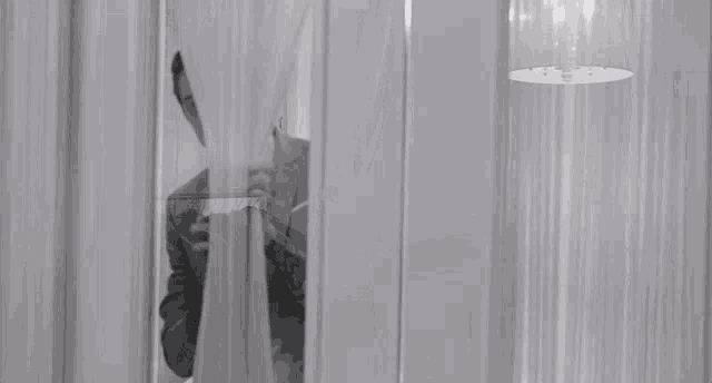 a black and white photo of a man peeking through a window curtain