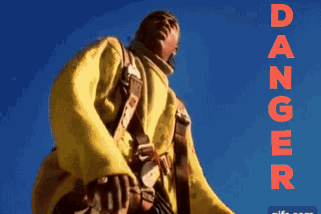 a man in a yellow jacket stands in the desert with the word danger written in red letters