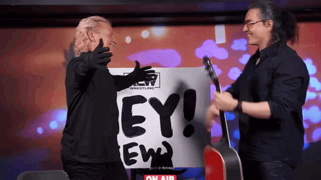 two men are hugging in front of a sign that says " ey ew "