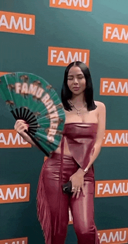 a woman in a red leather outfit is holding a fan in front of a wall that says famu