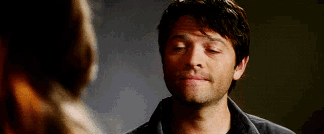 a man is making a funny face while looking at a woman in a dark room .