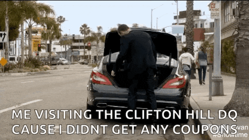 a man in a suit is opening the trunk of a car on a city street .