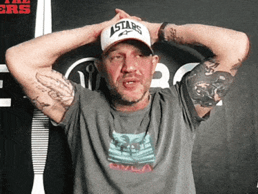 a man wearing a hat with the word astars on it is standing with his hands on his head .