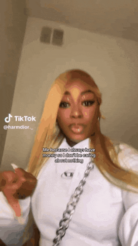 a woman with long blonde hair is wearing a white shirt and a silver chain