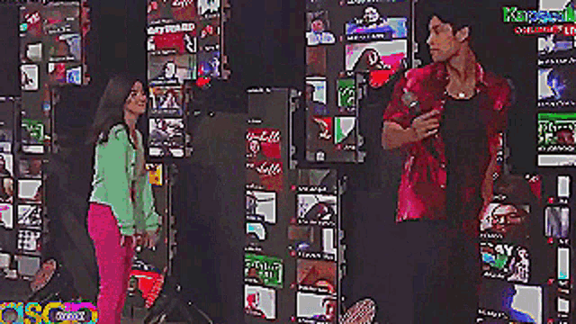 a man in a red shirt is standing next to a woman in a green jacket while talking into a microphone ..