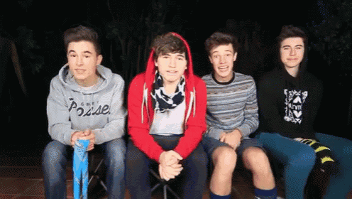 four young men are sitting in a row and one of them is wearing a hoodie that says ' pause ' on it