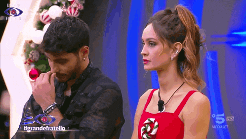 a woman in a red dress stands next to a man in a black shirt on a tv screen that says grandefratello