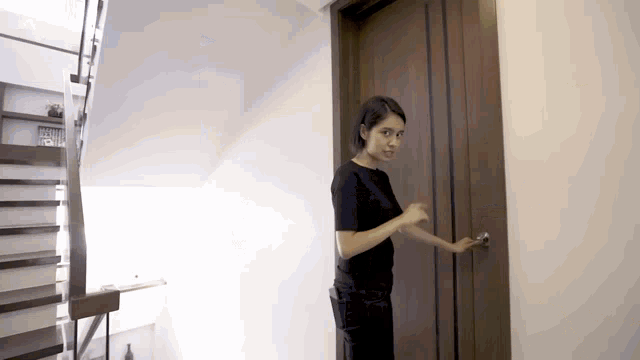 a woman in a black shirt opens a wooden door