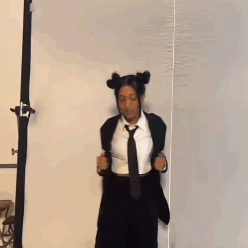 a woman in a suit and tie is dancing in front of a white curtain