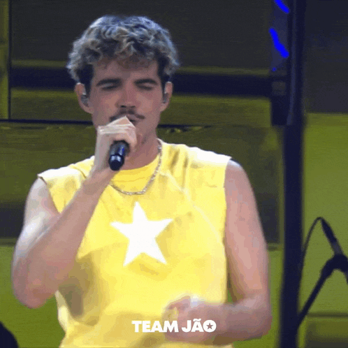 a man wearing a yellow shirt with a white star on it is singing into a microphone