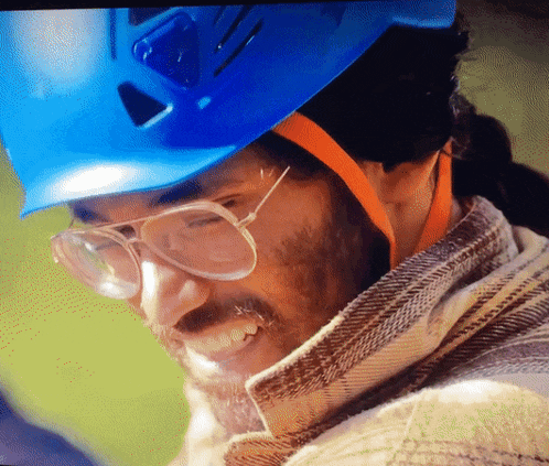 a man wearing glasses and a blue hard hat smiles