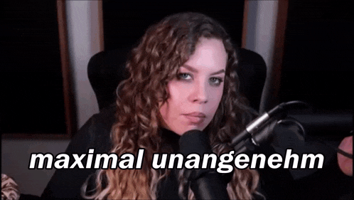 a woman is sitting in front of a microphone with the words `` maximal unangenehm '' written on her face .