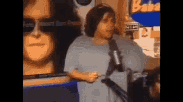 a woman is standing in front of a microphone in front of a poster of a man 's face