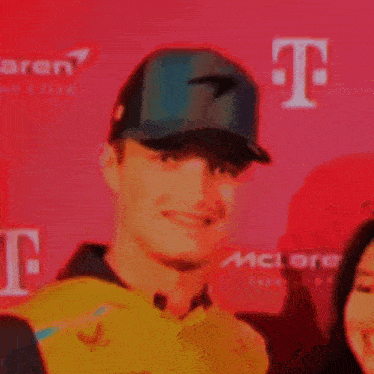 a man wearing a baseball cap is smiling in front of a red background with the letter t.