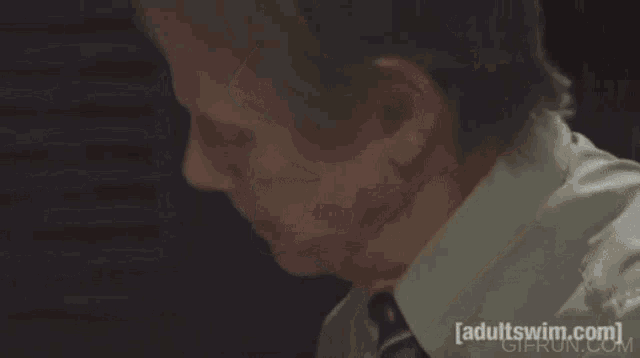 a man sitting at a desk looking at a cell phone with adultswim.com written on the bottom of the screen