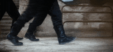 a person wearing a pair of black boots is walking on a dirt floor