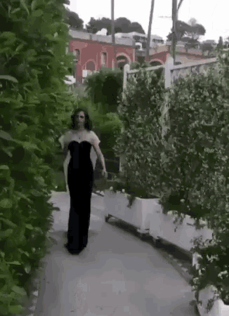 a woman in a black dress walking down a path