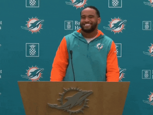 a man stands behind a podium with a dolphin logo on it