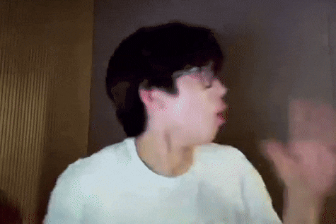a man wearing glasses and a white t-shirt is making a funny face and waving his hand .