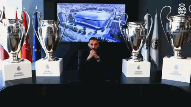 a man sits in front of several trophies including one that says ' champions league '