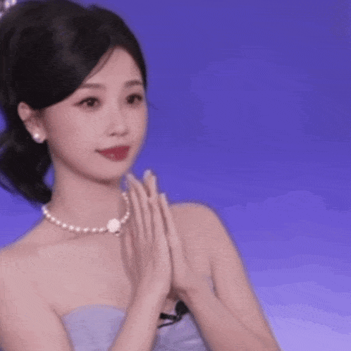 a woman wearing a pearl necklace and a strapless dress is applauding .