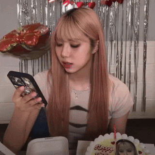a woman is looking at her phone in front of a cake that says " happy birthday "