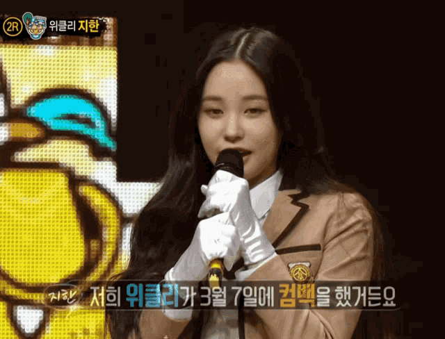 a girl in a school uniform holds a microphone in front of a screen that says ' 2r ' on it