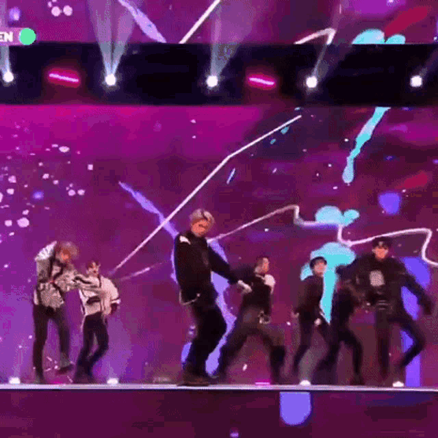 a group of people are dancing on a stage with a purple background .