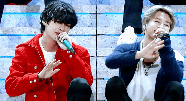 a man in a red jacket is singing into a microphone next to another man