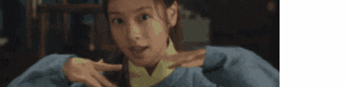 a woman in a blue sweater is making a funny face and pointing at something .