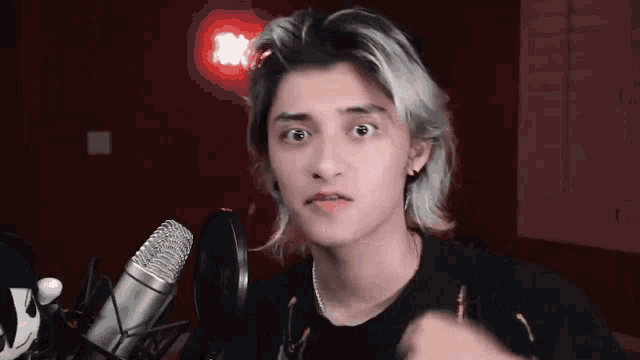 a young man with long blonde hair is standing in front of a microphone making a funny face .
