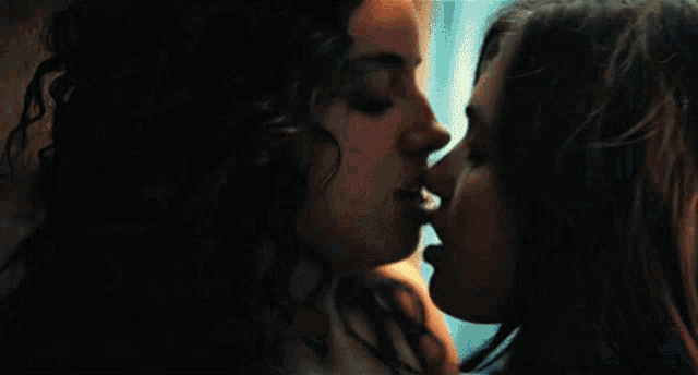 two women are kissing in front of a window in a kitchen